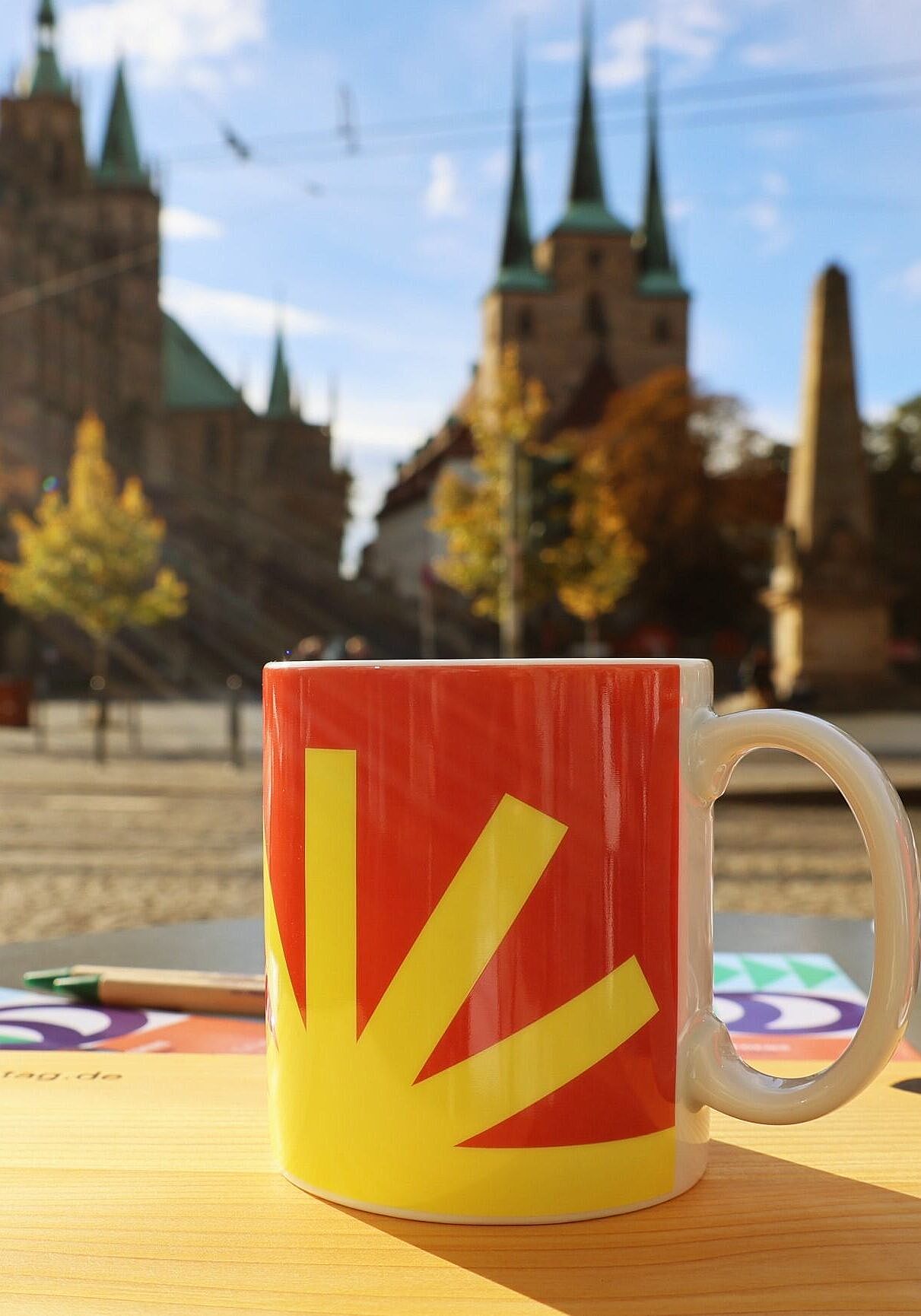 Die Katholikentag-Tasse auf einem Tisch vor dem im Hintergrund zu sehenden Erfurter Dom.